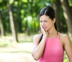 woman standing outside and holding her cheek in pain