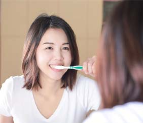 woman brushing her teeth in front of a mirror