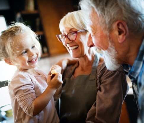 Older couple smiling at a child after dental implant tooth replacement